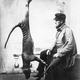 A bagged thylacine strung up beside a hunter.